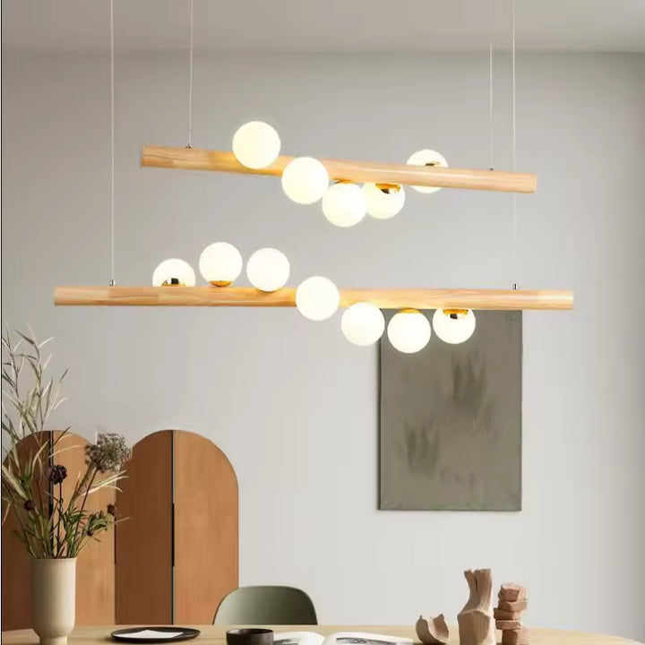 Deux suspensions linéaires en bois clair à globes lumineux composent un décor japandi, naturel et contemporain.