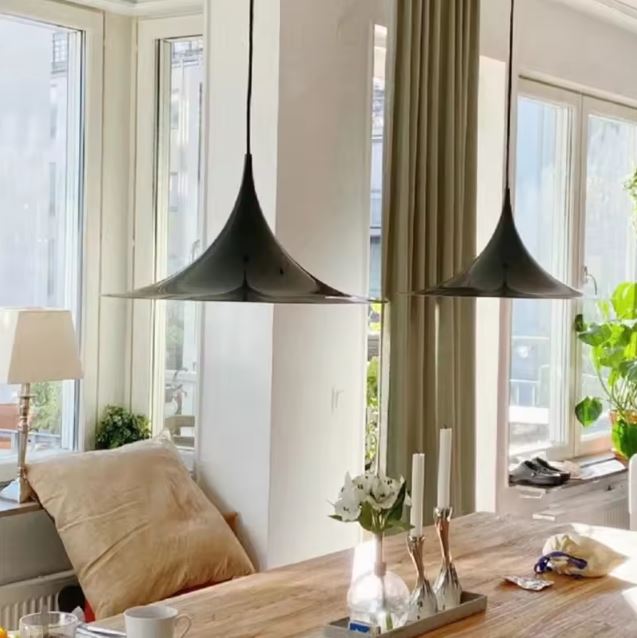 Duo de suspensions noires à large disque au-dessus d’une table en bois, entre modernisme des années 50 et design italien.