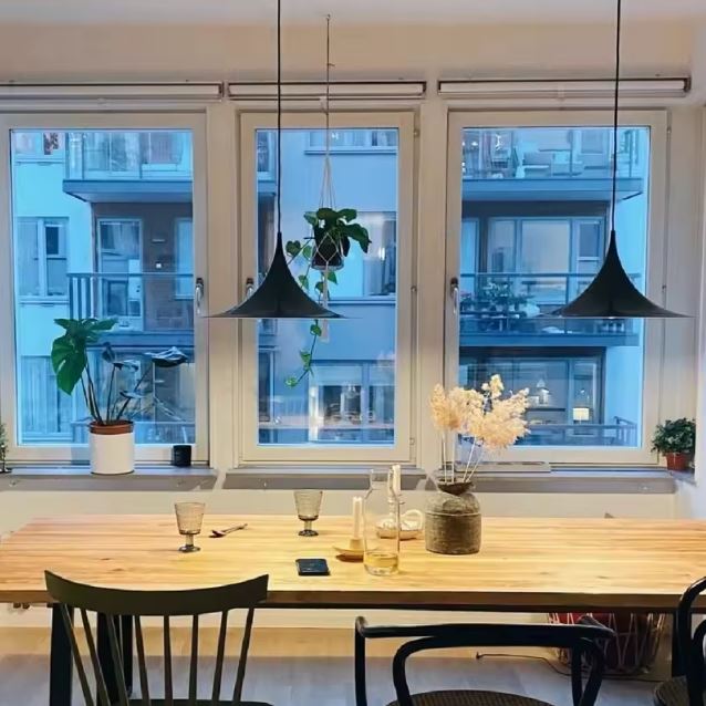 Deux suspensions noires aux lignes fines au-dessus d’une table en bois, ambiance scandinave et moderniste.