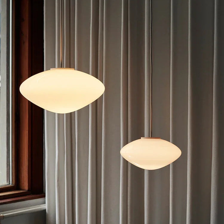 Deux suspensions en verre opalin au design scandinave épuré, suspendues dans une chambre moderne.