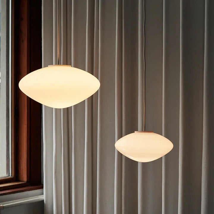 Deux suspensions en verre opalin au design scandinave épuré, suspendues dans une chambre moderne.