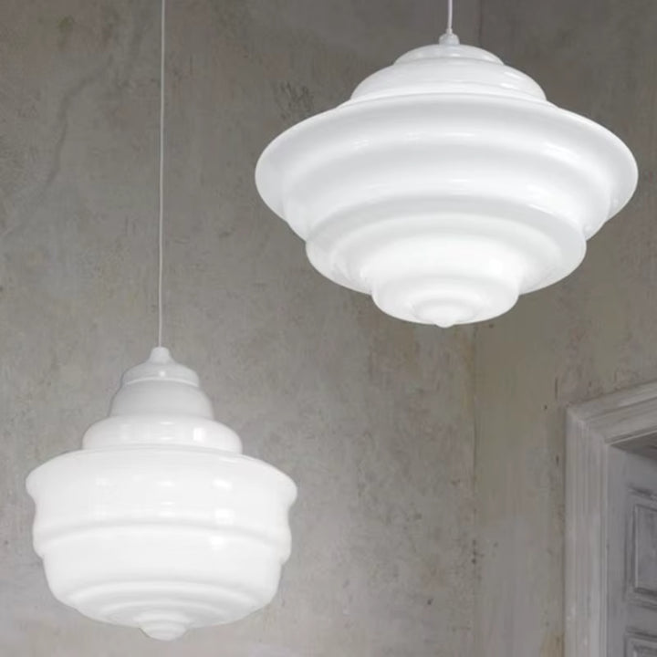 Deux suspensions en verre blanc opalin aux courbes sculpturales et reliefs concentriques, dans un décor minimaliste.
