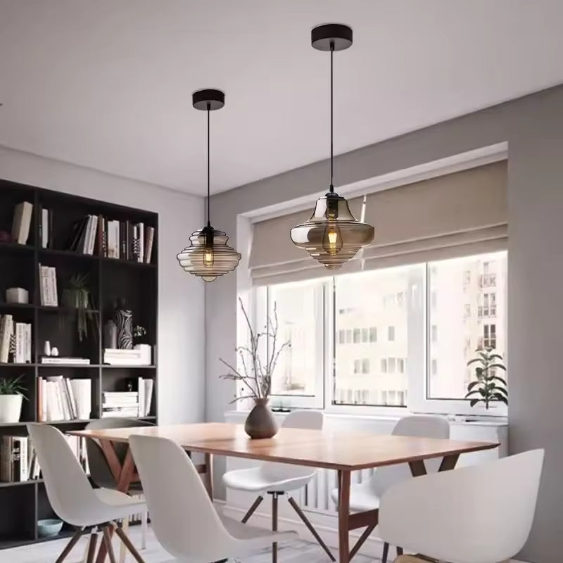 Deux suspensions en verre fumé aux anneaux superposés, éclairant une table en bois dans une salle à manger scandinave.