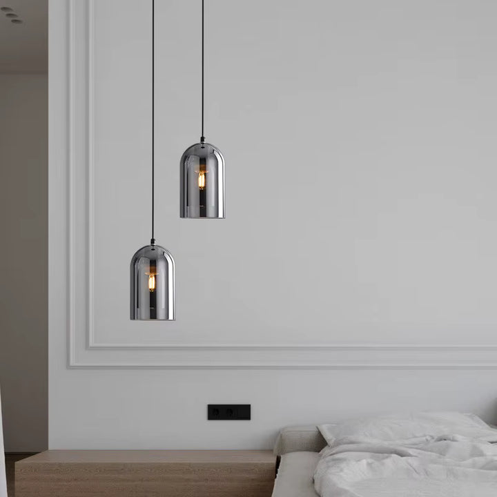 Deux suspensions en verre fumé à hauteur décalée, apportant une touche design et industrielle à une chambre épurée.