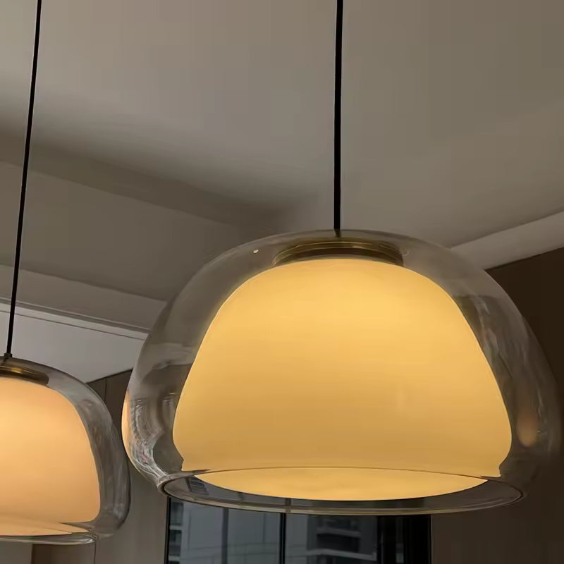 Deux suspensions en verre clair et opalin diffusent une lumière chaude dans un décor au style design et chaleureux