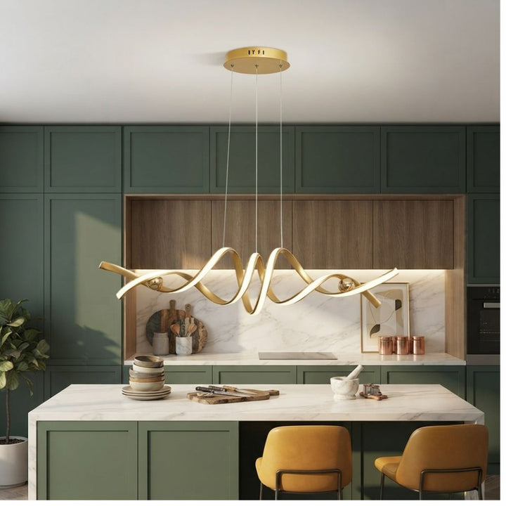 Longue suspension dorée illuminant un îlot de cuisine moderne en bois et vert sauge pour une ambiance conviviale.