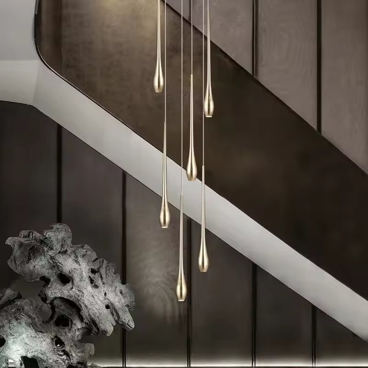 Dans un escalier contemporain, des gouttes dorées élancées forment un lustre cascade au rendu sculptural