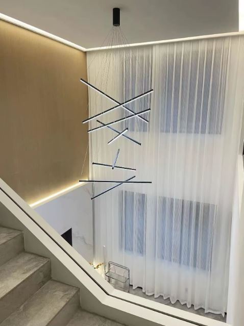 Grande suspension cage d’escalier LED, suspendue dans un intérieur architectural à la fois épuré et contemporain.