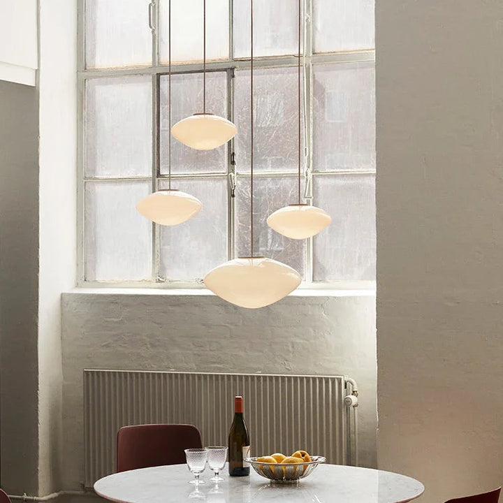 Grappe de suspensions en verre opalin au-dessus d'une table, créant un éclairage harmonieux et moderne.
