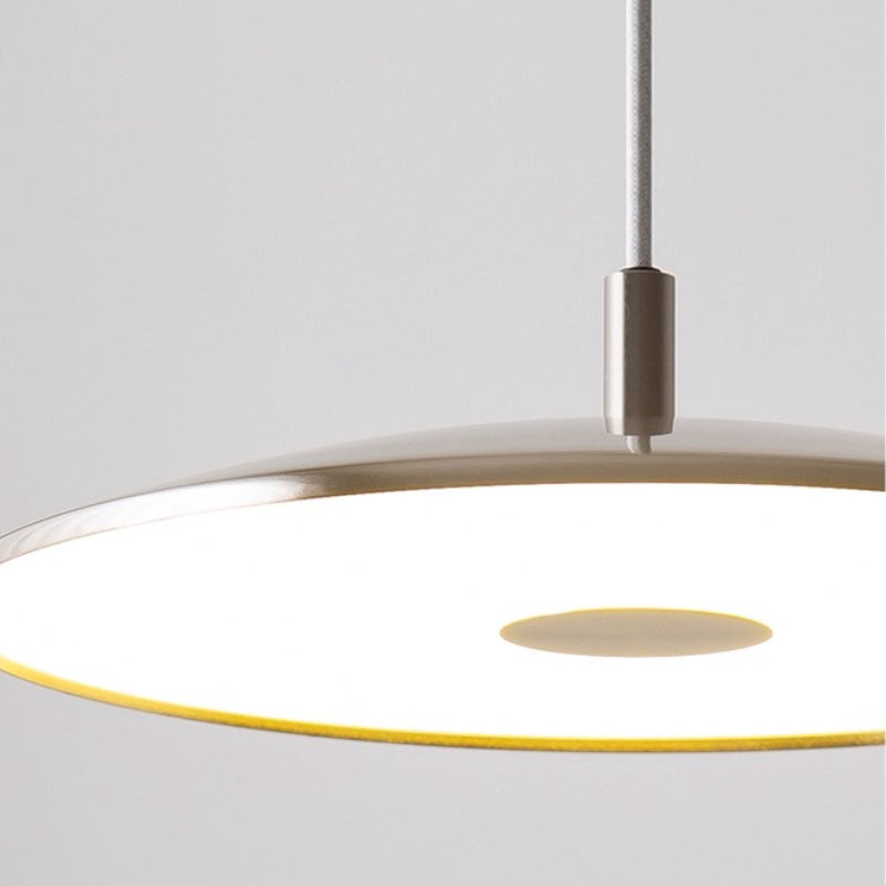 Gros plan sur le halo lumineux led diffusé sous la suspension plate en métal brossé.