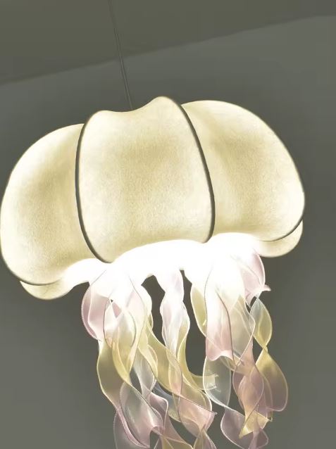 Gros plan sur une suspension méduse blanche aux filaments irisés, avec un rendu féerique et organique.