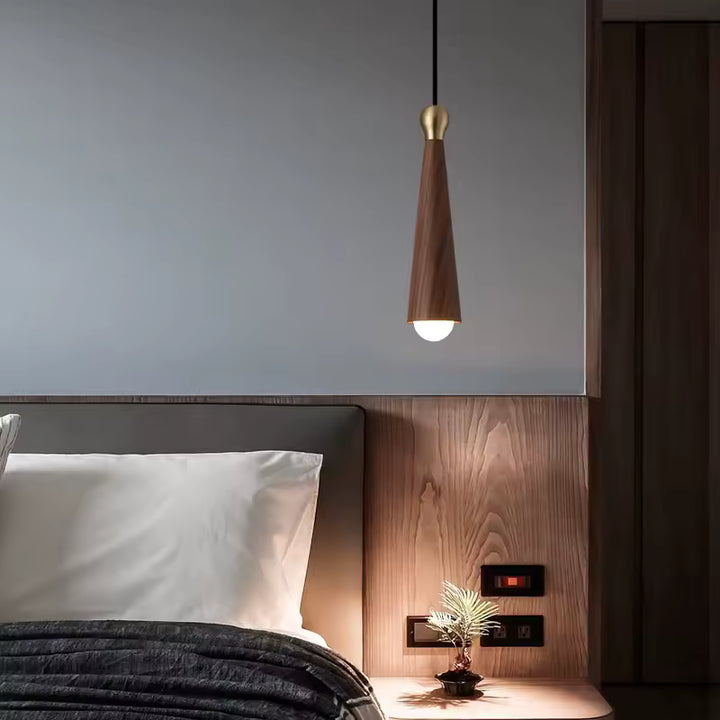 Au-dessus du chevet, cette lampe suspendue en bois de noyer noir et laiton dévoile une silhouette conique chaleureuse et raffinée