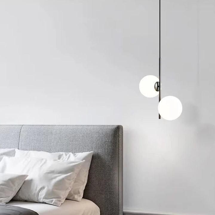Lampe suspension minimaliste à boules lumineuses suspendue près d'une tête de lit grise.