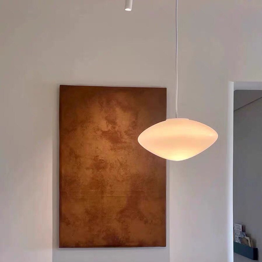 Lampe suspension minimaliste en verre opalin, ajoutant une note design à un mur décoré d'un tableau.