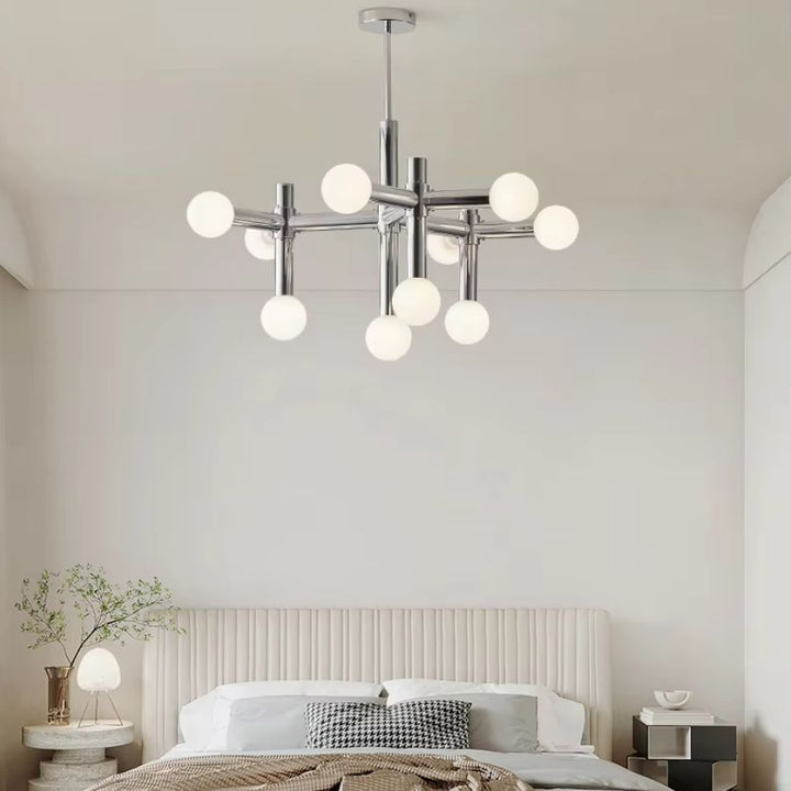 Luminaire chromé à globes opalins suspendu dans une chambre épurée, au style moderne et mid-century