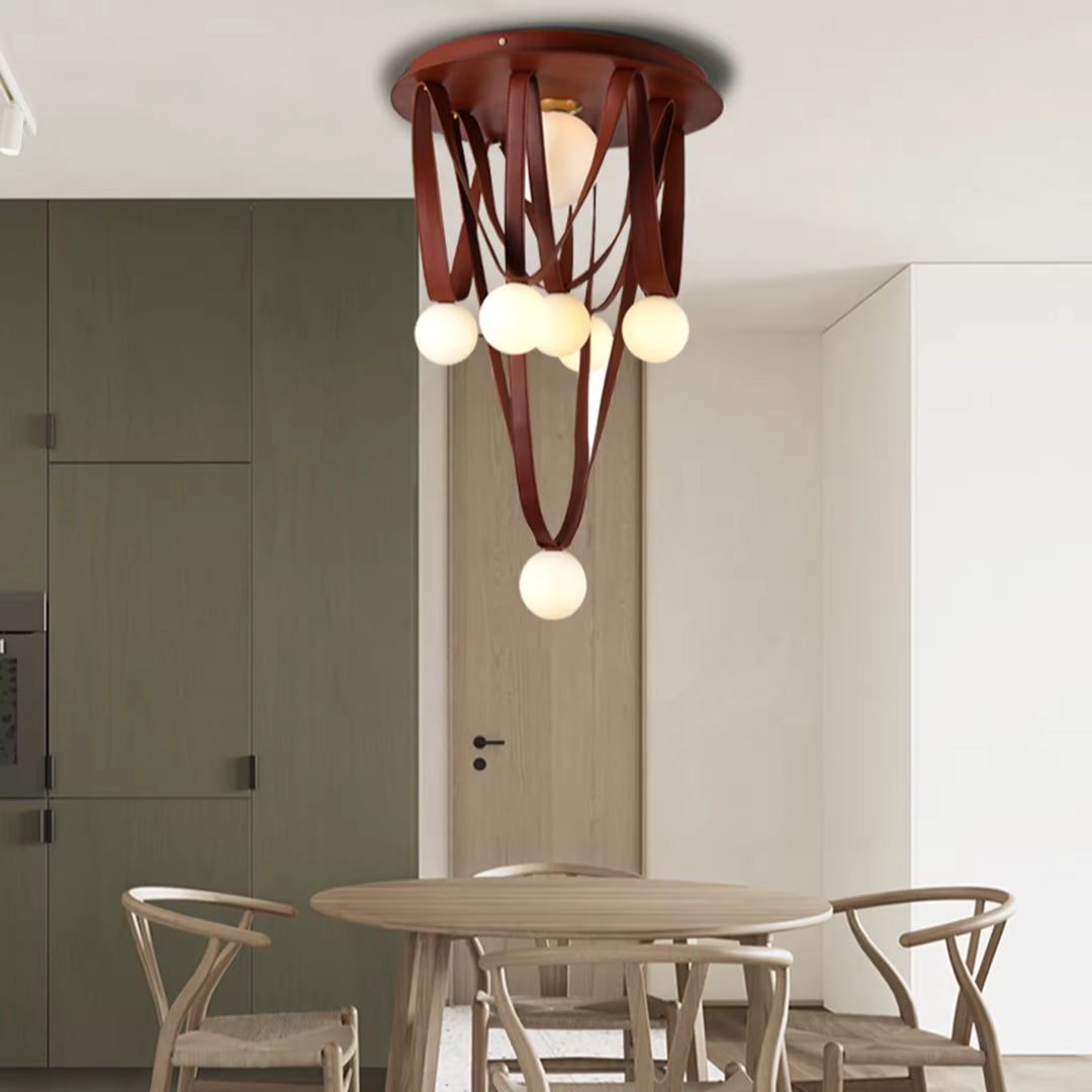 Dans une salle à manger épurée, le lustre en cuir brun et globes opalins apporte une présence organique et sculpturale.