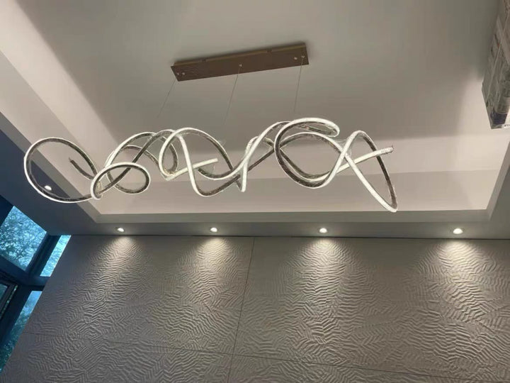 Luminaire design ondulé fixé sur un haut plafond, mettant en valeur des volumes architecturaux.