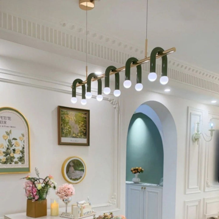 Luminaire linéaire design vert et doré à arches suspendu dans un intérieur décoré avec des cadres muraux.