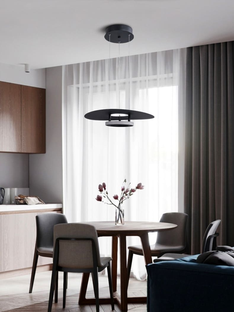Luminaire disque flottant noir illuminant une table ronde dans un salon moderne.