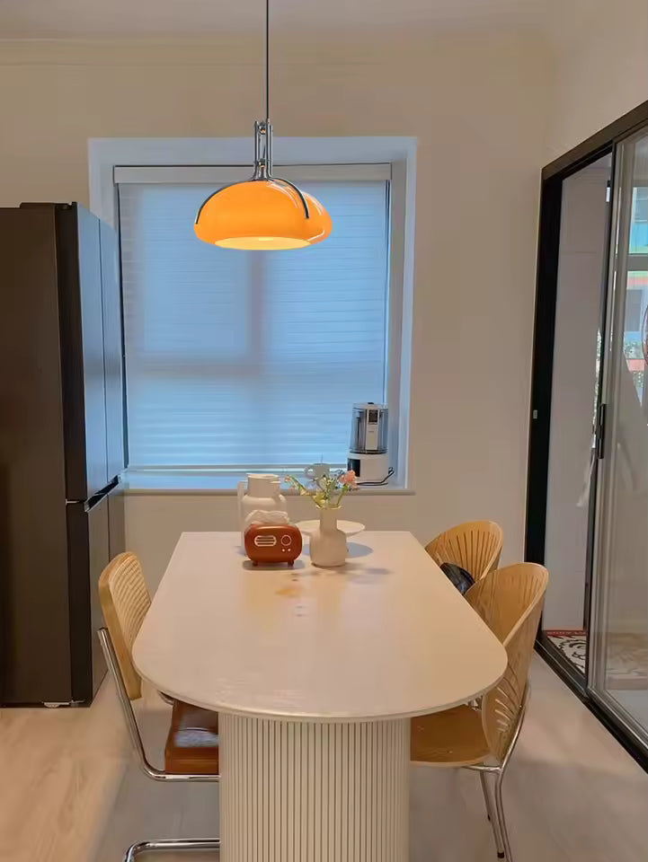 Luminaire dôme orange à détails chromés, installé au-dessus d’une table dans une salle à manger rétro moderne