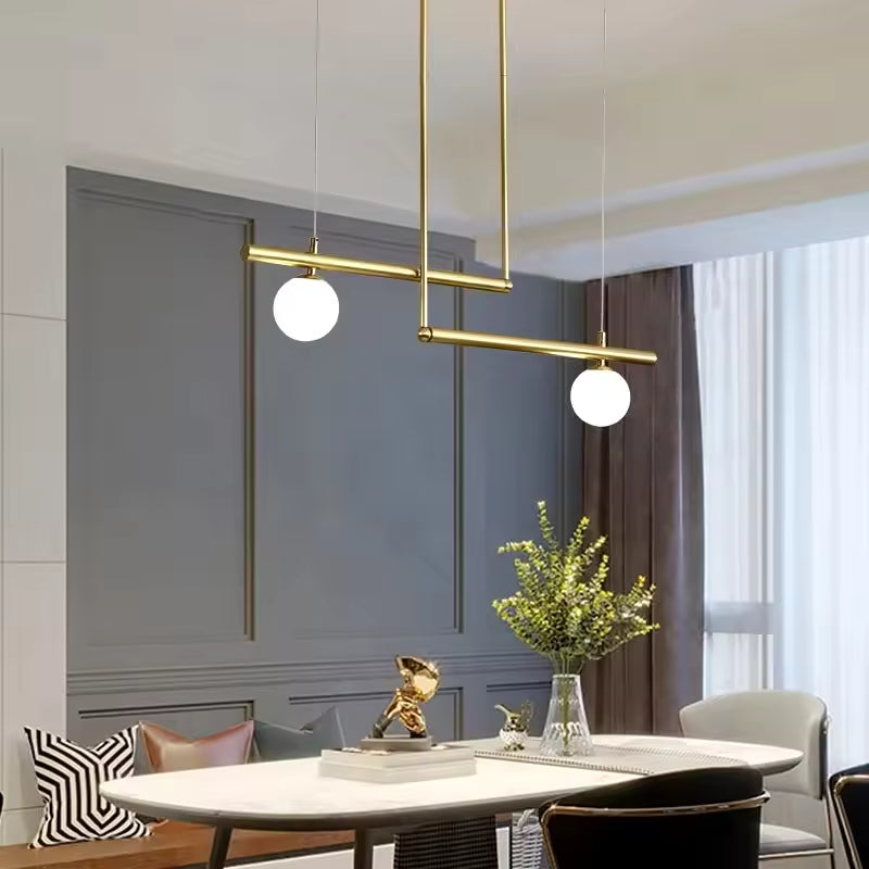 Luminaire doré à lignes décalées et deux globes opalins, mis en scène dans une salle à manger élégante et moderne