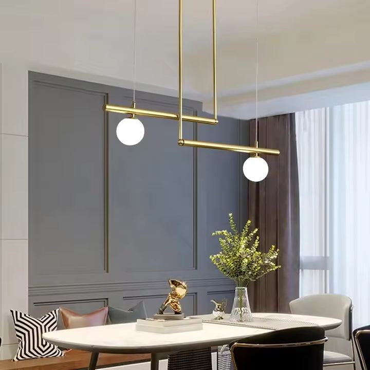 Luminaire doré à lignes décalées et deux globes opalins, mis en scène dans une salle à manger élégante et moderne