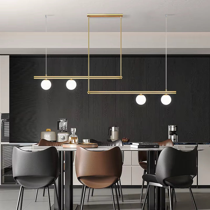 Luminaire doré à lignes décalées et quatre globes opalins, structurant une cuisine contemporaine au style graphique