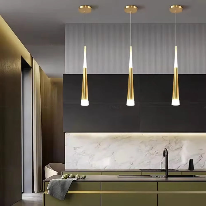 Dans une cuisine moderne, trois luminaires LED dorés au profil effilé soulignent élégamment l’îlot central