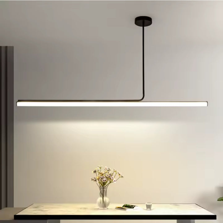 Un luminaire LED tubulaire noir au style minimaliste éclaire une table avec une ligne lumineuse fine et contemporaine.