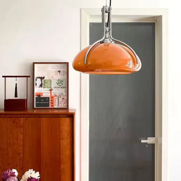Lampe suspendue orange à armature chromée dans un décor vintage, avec silhouette Space Age typique des années 60 et 70