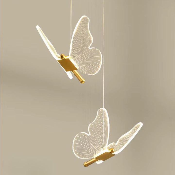 Deux papillons aux ailes transparentes et dorées forment un luminaire suspendu délicat au style aérien
