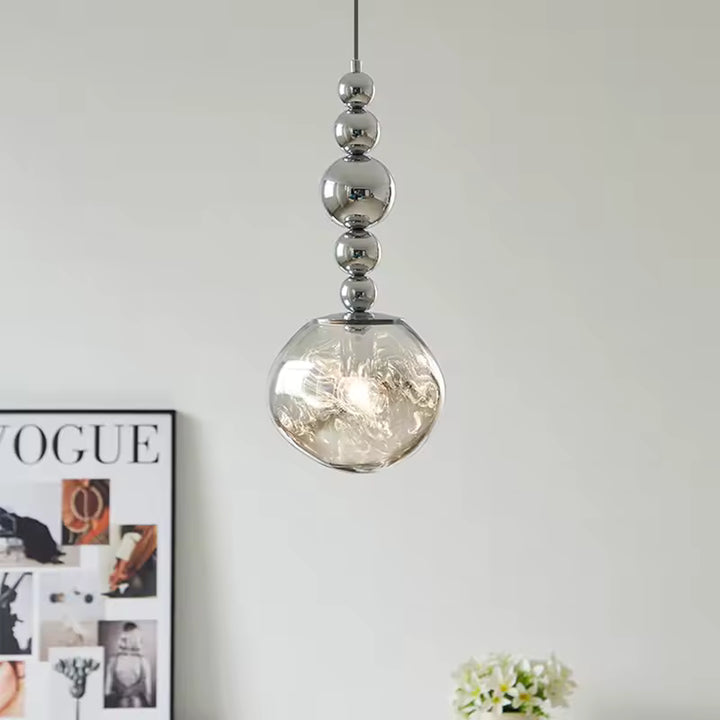 Dans un intérieur moderne, ce luminaire à sphères chromées révèle un globe transparent texturé aux reflets lumineux
