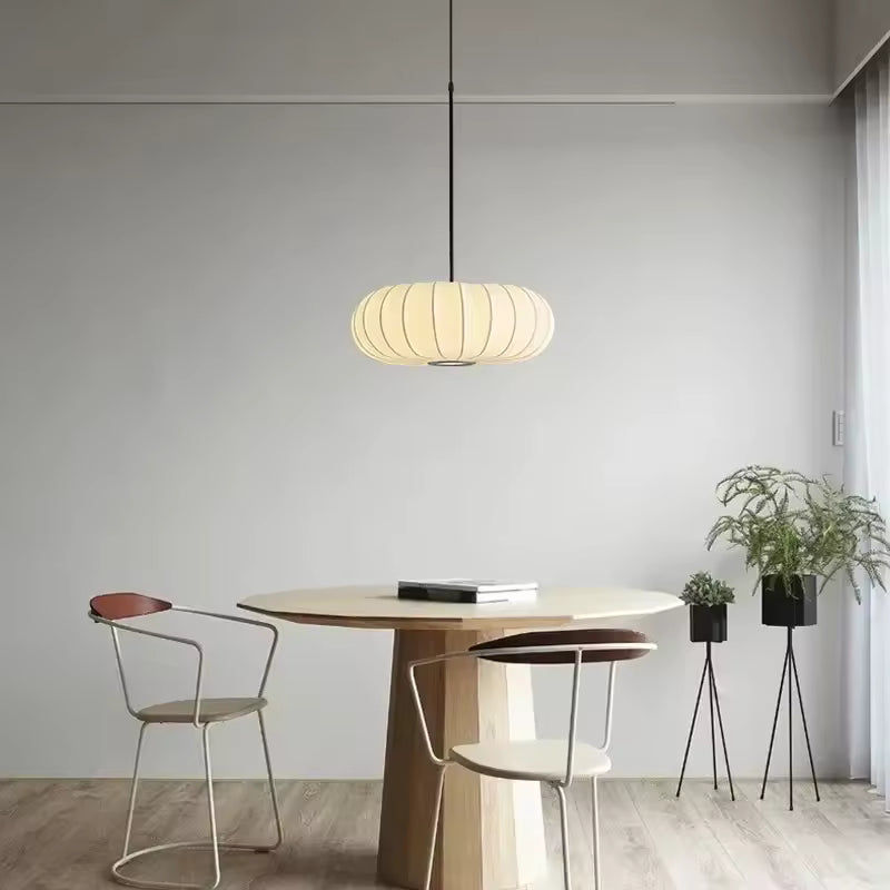 Luminaire suspendu en tissu ivoire nervuré au-dessus d’une table, dans une salle à manger minimaliste et japandi