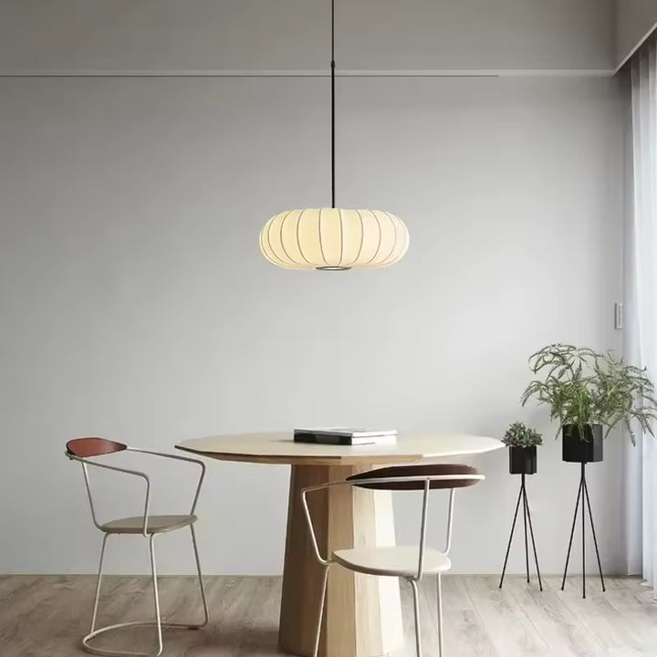 Luminaire suspendu en tissu ivoire nervuré au-dessus d’une table, dans une salle à manger minimaliste et japandi