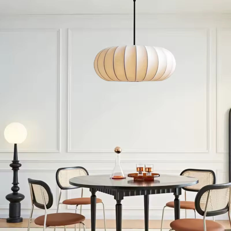 Luminaire en tissu ivoire nervuré au-dessus d’une table ronde, dans une salle à manger japandi élégante