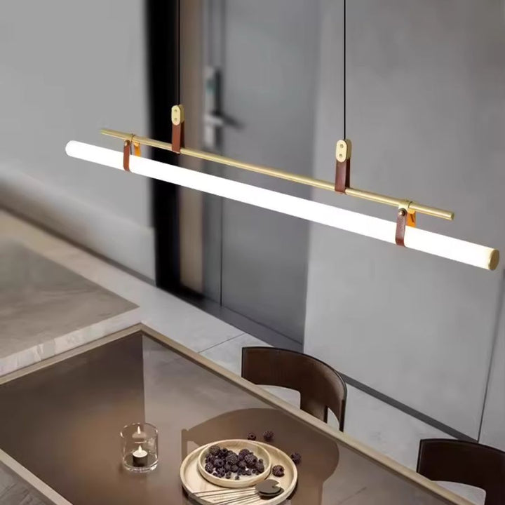 Luminaire suspendu tube LED doré à attaches en cuir, suspendu au-dessus d’une table dans un intérieur contemporain épuré