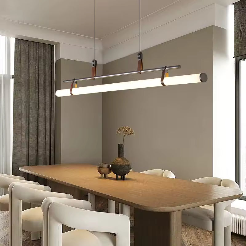 Luminaire suspendu noir à tube néon LED à attaches en cuir, suspendu au-dessus d’une grande table en bois dans un décor contemporain