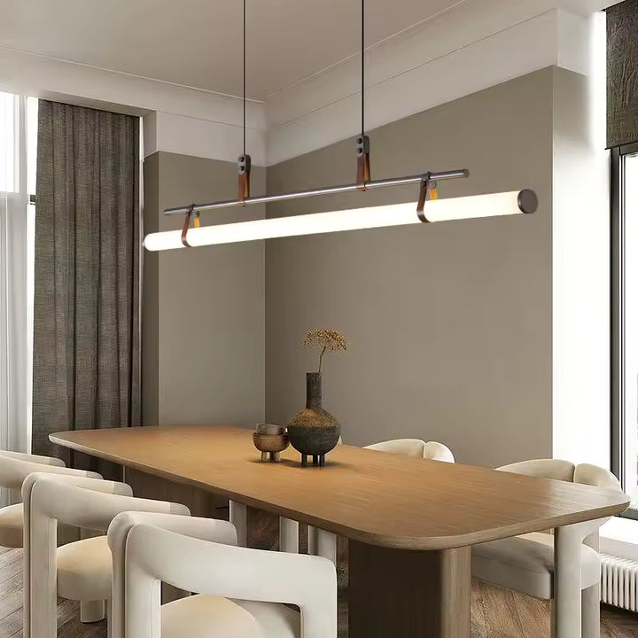 Luminaire suspendu noir à tube néon LED à attaches en cuir, suspendu au-dessus d’une grande table en bois dans un décor contemporain