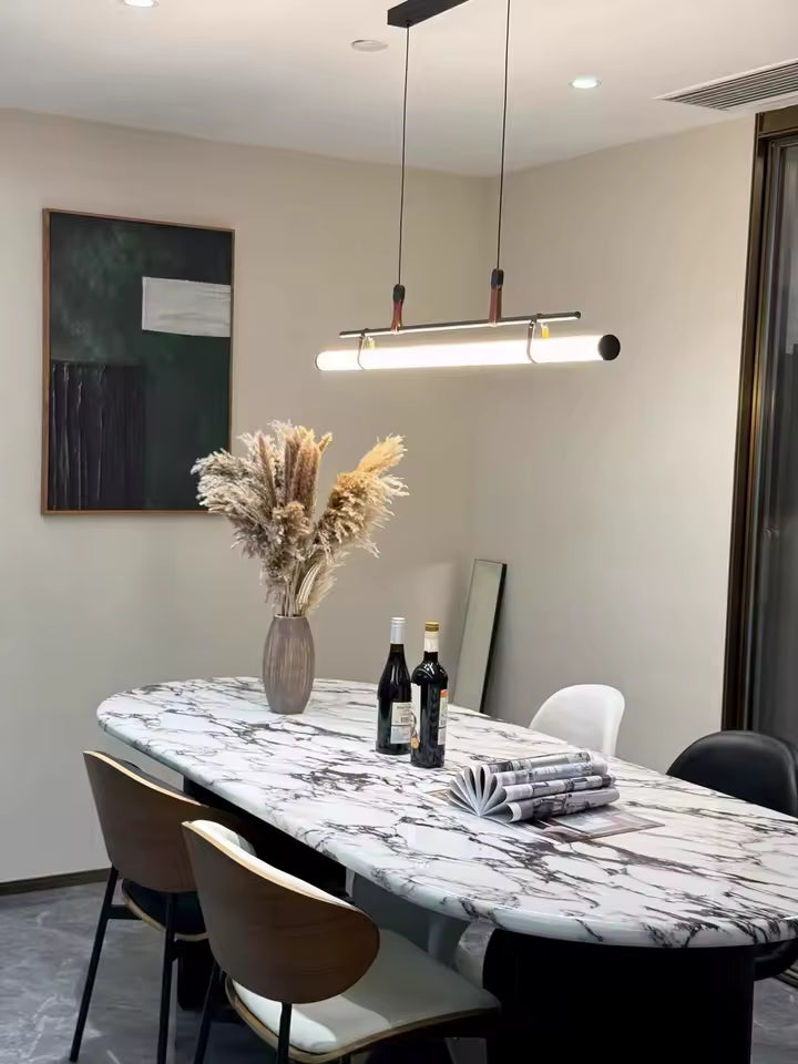 Luminaire tube LED noir à attaches en cuir, suspendu au-dessus d’une table en marbre dans une salle à manger élégante