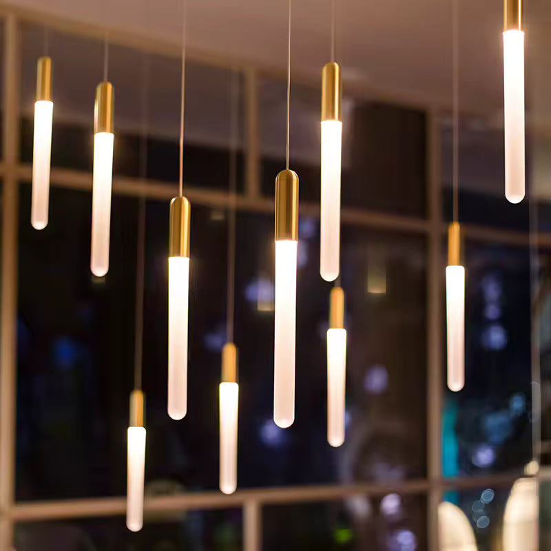Devant une baie vitrée, plusieurs tubes lumineux dorés composent un luminaire contemporain à l’allure raffinée