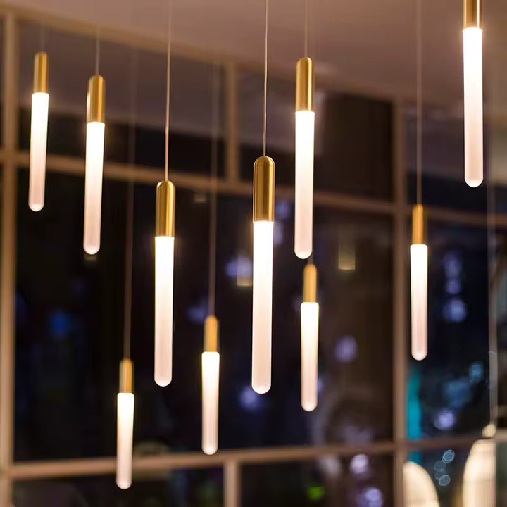 Devant une baie vitrée, plusieurs tubes lumineux dorés composent un luminaire contemporain à l’allure raffinée