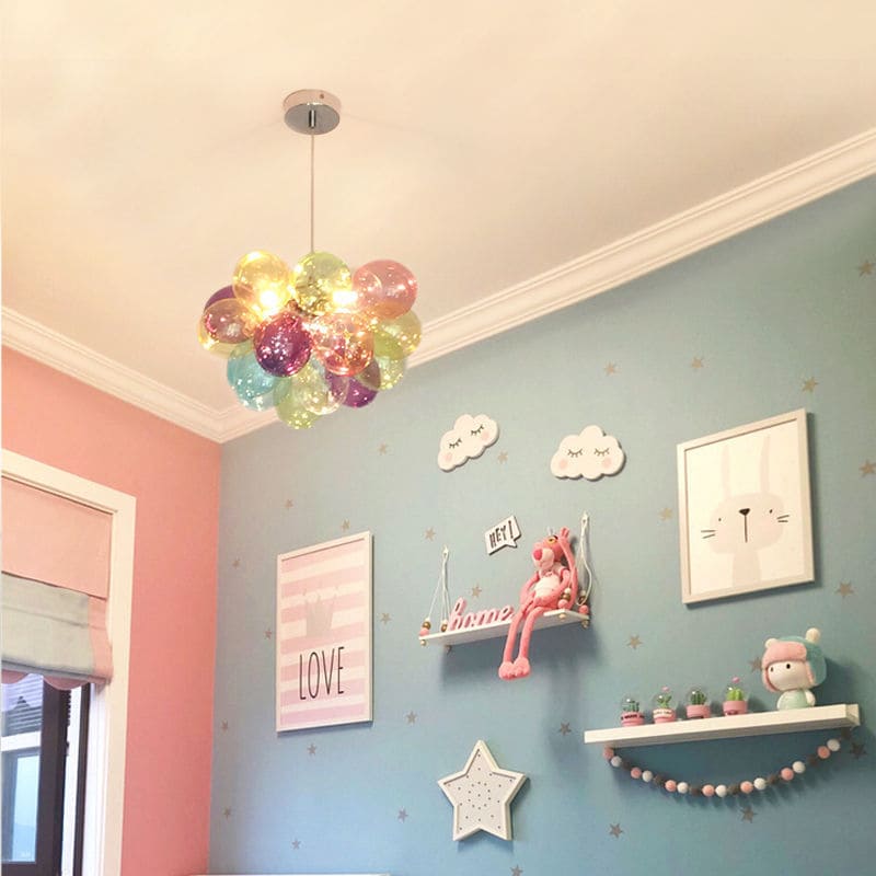 Luminaire ludique en verre translucide coloré suspendu dans une chambre d'enfant douce et ordonnée.