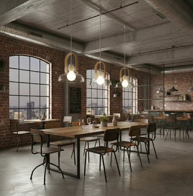 Au-dessus d’une grande table, trois luminaires en bois clair et verre soufflé renforcent l’esprit loft industriel du lieu