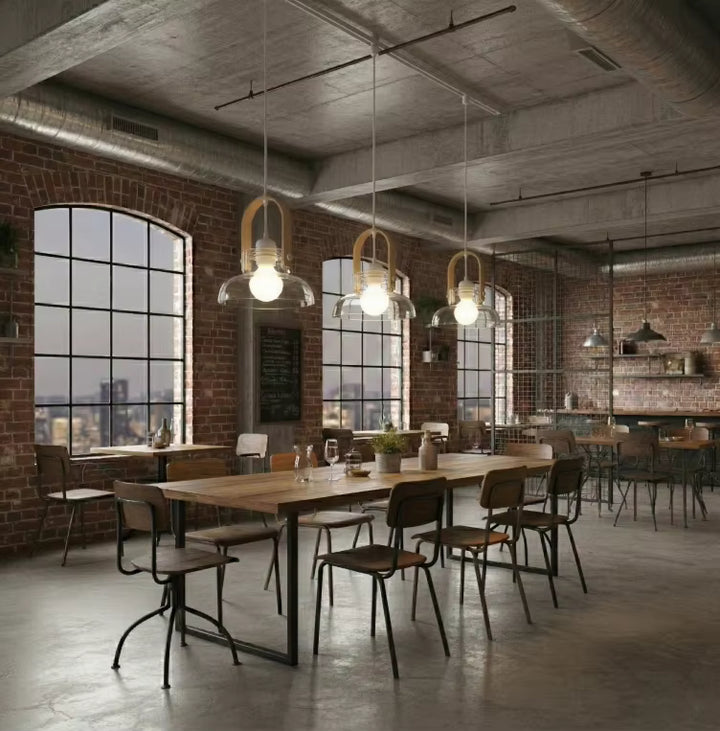 Au-dessus d’une grande table, trois luminaires en bois clair et verre soufflé renforcent l’esprit loft industriel du lieu
