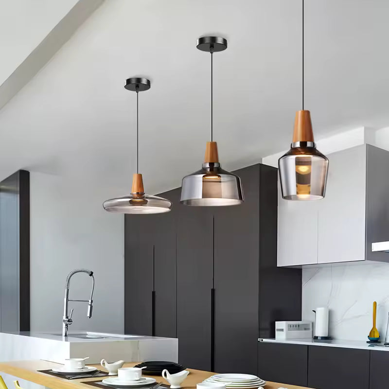 Dans une cuisine contemporaine, trois luminaires en verre fumé et bois affichent des silhouettes sculpturales variées