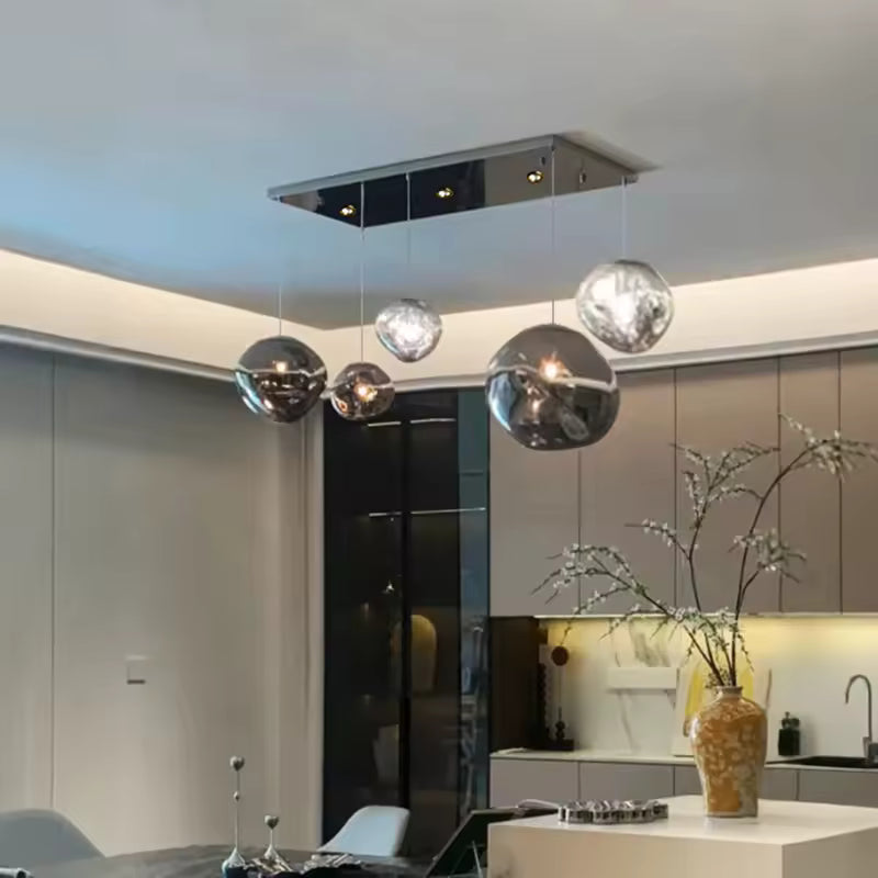 Au-dessus d'un îlot de cuisine moderne, cinq globes en verre fumé et transparent forment une suspension au style sculptural.