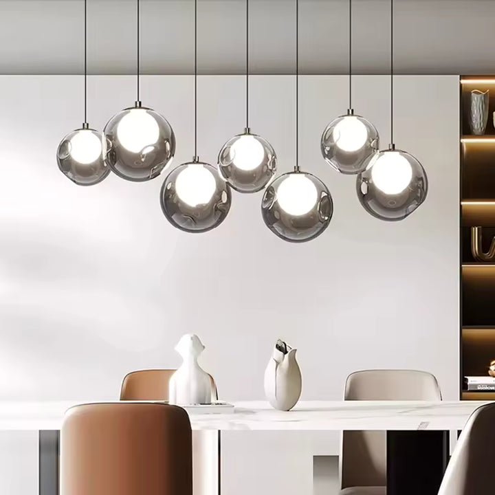 Une suspension linéaire à sept sphères transparentes et cœurs lumineux éclaire une salle à manger au style contemporain.
