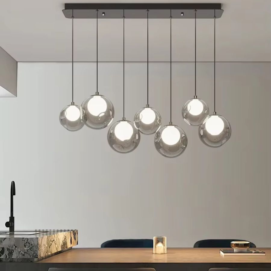 Suspendu au-dessus d'une table en bois, ce lustre minimaliste à sept globes transparents diffuse une lumière blanche douce.