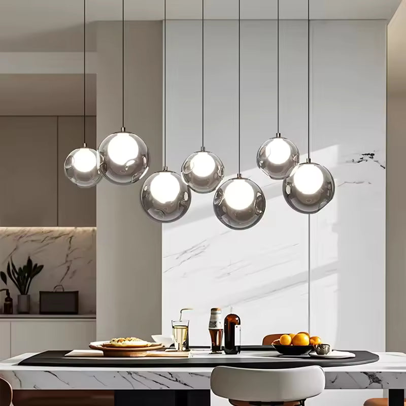 Sept sphères transparentes à cœur lumineux composent une suspension linéaire élégante au-dessus d'un îlot en marbre.