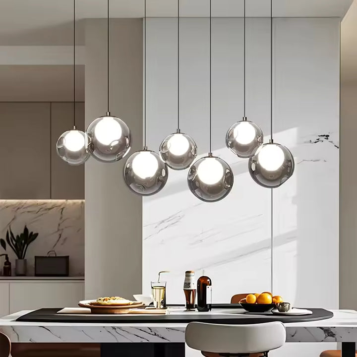 Sept sphères transparentes à cœur lumineux composent une suspension linéaire élégante au-dessus d'un îlot en marbre.